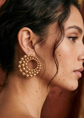 Close-up of a person wearing gold hoop earrings with a blurred background