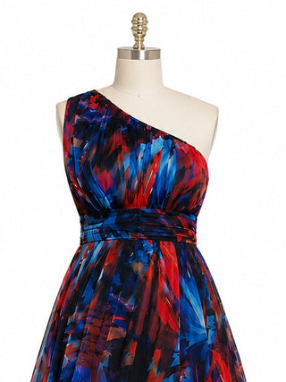 A one-shoulder dress with a vibrant abstract brushstroke pattern in red, blue, and black, displayed on a cream-colored dress form mannequin against a white background.