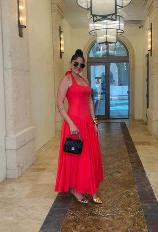 Woman in a red dress standing in a hallway with marble walls and a chandelier.