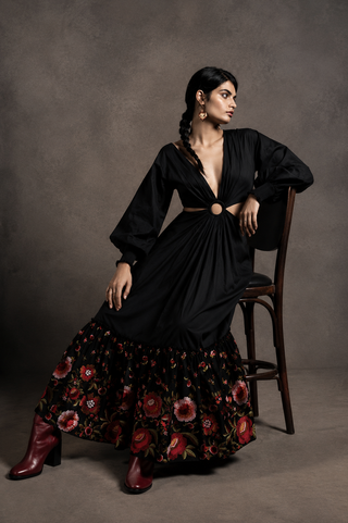 Woman in a black dress with floral skirt sitting on a chair against a gray background