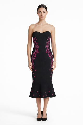 Woman wearing a black strapless dress with pink floral patterns on a white background