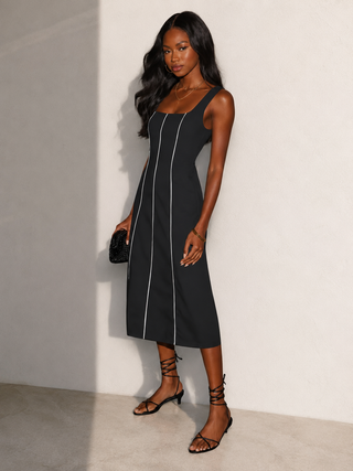 Woman wearing a black dress with white piping against a plain background