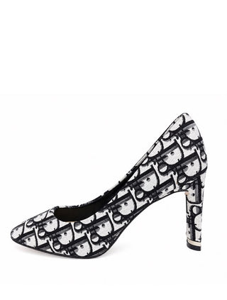 A single high-heeled pump shoe featuring a black and white repeating monogram pattern, shown from a side profile view against a plain white background.