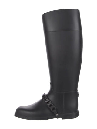 A single black knee-high rubber rain boot with a decorative chain detail around the ankle, shown from a side profile on a white background.