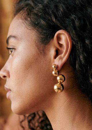 Close-up of a person wearing gold earrings with a blurred background