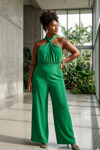 Woman wearing a green jumpsuit standing in an indoor setting with plants in the background