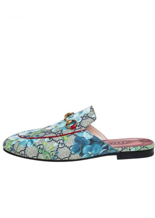 A Gucci slip-on mule loafer featuring a blue and green floral print over the brand's signature GG monogram canvas, accented with a gold horsebit detail on the vamp and a pink insole.