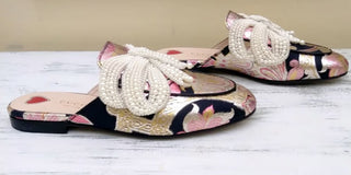 Floral-patterned slippers with pearl embellishments on a light wooden surface