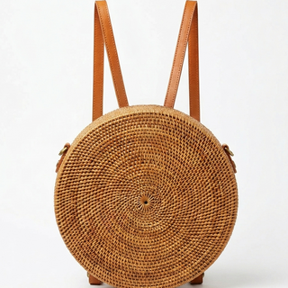 Round woven bag with brown leather straps on a white background