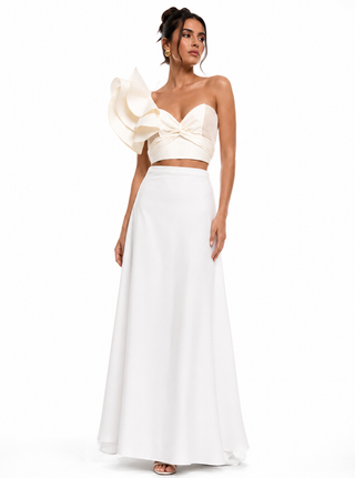Woman wearing a white one-shoulder top and long white skirt on a white background
