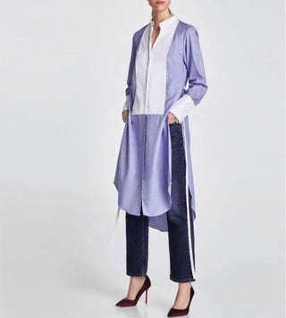 Person wearing a long light purple cardigan over a white shirt with dark jeans on a white background
