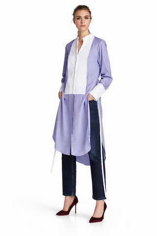 Woman wearing a long light purple cardigan over a white shirt with dark jeans on a white background