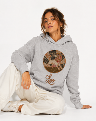 Woman wearing a gray hoodie with a 'Leo' design sitting on a white background