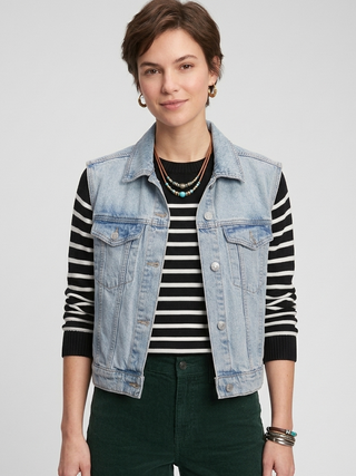 Woman wearing a denim vest over a striped shirt with a plain background