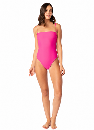 A woman modeling a bright pink one-piece swimsuit with thin shoulder straps and a square neckline, photographed against a plain white background.