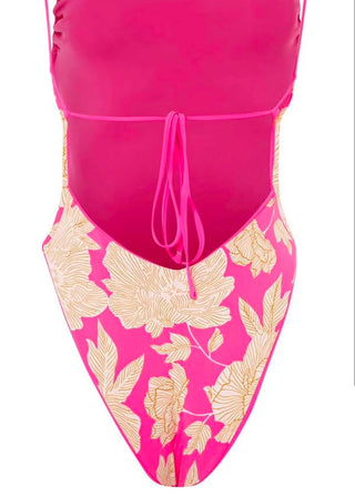 A close-up of a one-piece swimsuit in bright pink, featuring a solid pink upper section with a front tie closure and a lower section with a beige floral print on a pink background.