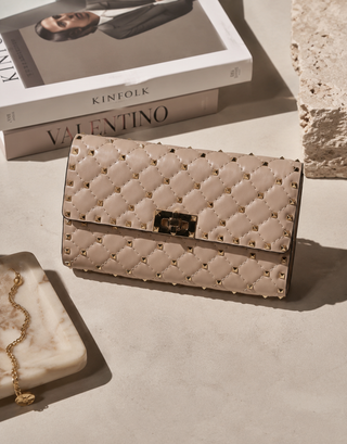 Quilted beige wallet with studded details on a light surface, with 'Kineolk' and 'Valentino' books in the background.