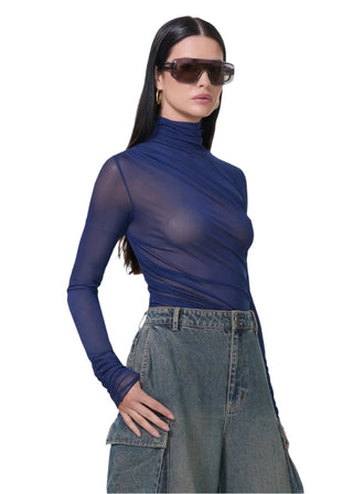 Woman wearing a sheer blue top and denim skirt with sunglasses on a white background