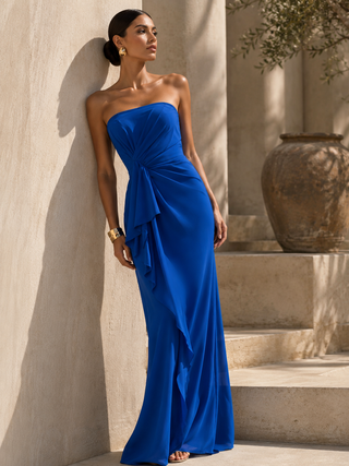 Woman in a blue strapless gown standing against a stone wall.