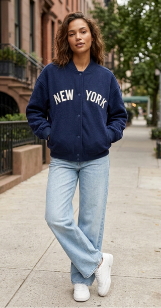 Person wearing a navy blue 'New York' jacket on a city street.