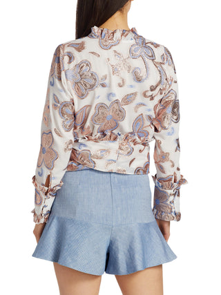 Woman wearing a patterned blouse and denim shorts on a white background