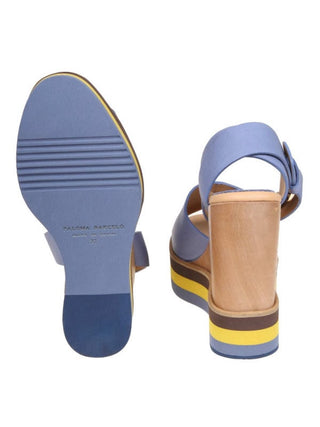 A pair of women's platform sandals shown from the back, displaying the blue sole and the stacked platform heel with blue, tan, brown, and yellow layers. The sandals feature a light blue leather strap with a side buckle and a tan footbed.