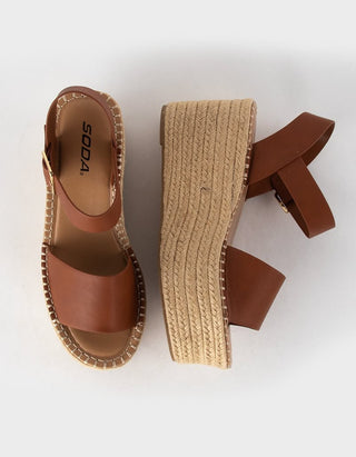 A pair of wedge espadrille sandals by SODA, shown from top and side angles on a clean white background. The sandals feature tan leather straps, a braided jute platform wedge, and a gold-tone buckle.