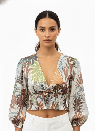 Woman wearing a tropical leaf patterned blouse with white pants on a white background