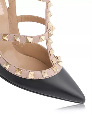 A close-up of a pointed-toe high heel shoe with a black leather lower section and a light beige upper section decorated with gold pyramid studs, on a white background.