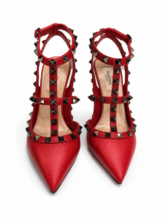 A pair of red pointed-toe high heels with studded straps, shown from a top-down view on a white background. The brand name 'VALENTINO' is visible on the insole.