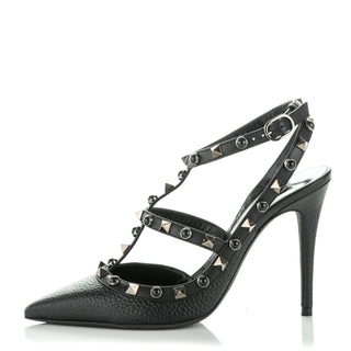 A black pebbled leather high-heeled pump with an ankle strap, pointed toe, and silver pyramid studs, shown from a side profile on a white background.