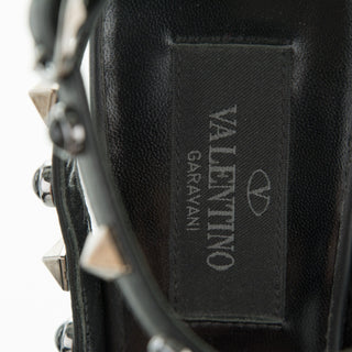Close-up of a black leather handbag showing the interior label with 'VALENTINO GARAVANI' text and logo, alongside visible silver-tone studs and trim.