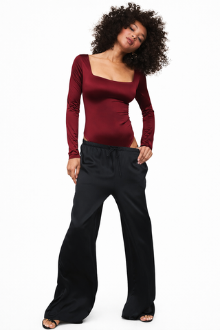 Woman wearing a burgundy long-sleeve top and black pants on a white background