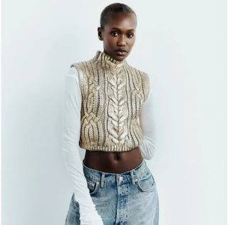 Person wearing a beige knitted vest over a white shirt with blue jeans on a light gray background