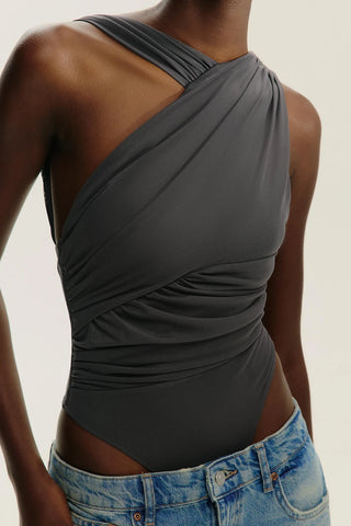 Person wearing a gray halter top and blue jeans on a neutral background