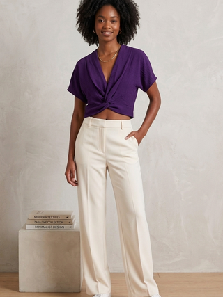 Woman wearing a purple top and white pants standing against a plain background